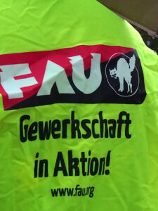 Gelbe Streikweste mit aufgedrucktem FAU Logo und dem Text „Gewerkschaft in Aktion!“